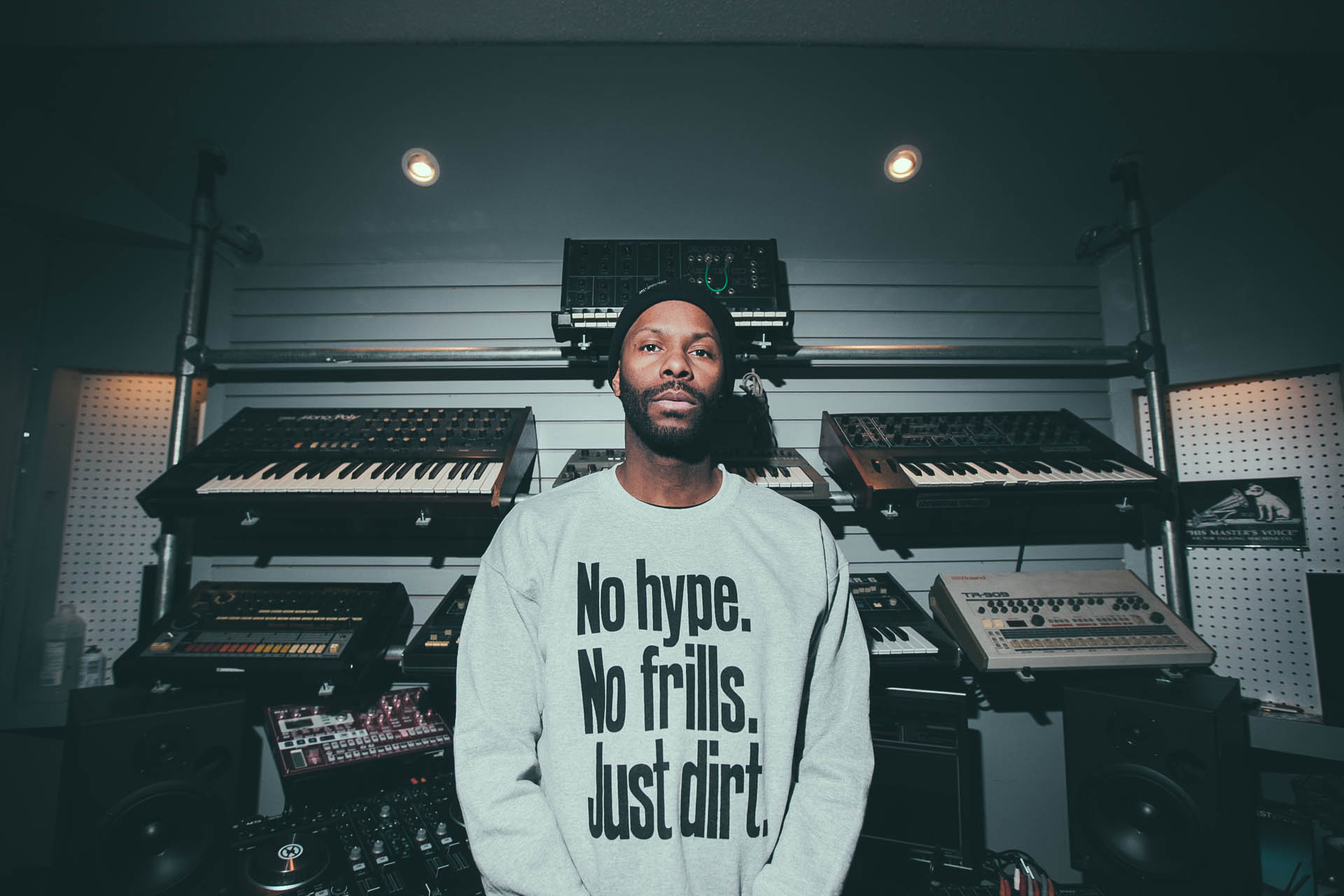 Waajeed standing in front of a collection of synthesizers, looking straight into the camera